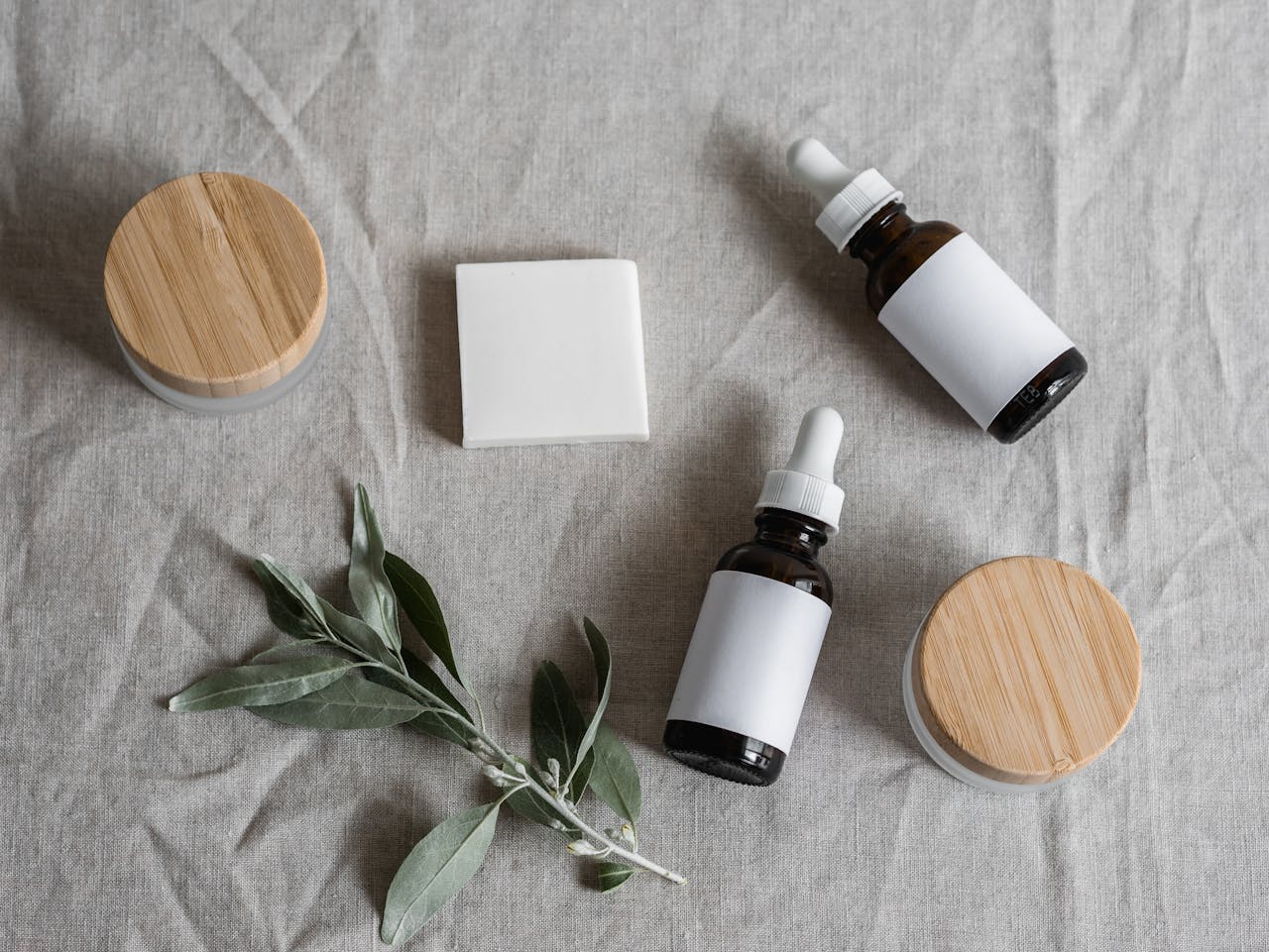hero-img-01 Top view of skincare products with a natural theme, featuring bottles, jars, and a plant on linen cloth.