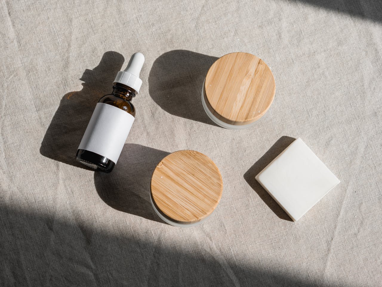 hero-img-02 Flat lay of natural skincare products with wooden lids on a linen fabric background, perfect for eco-friendly branding.
